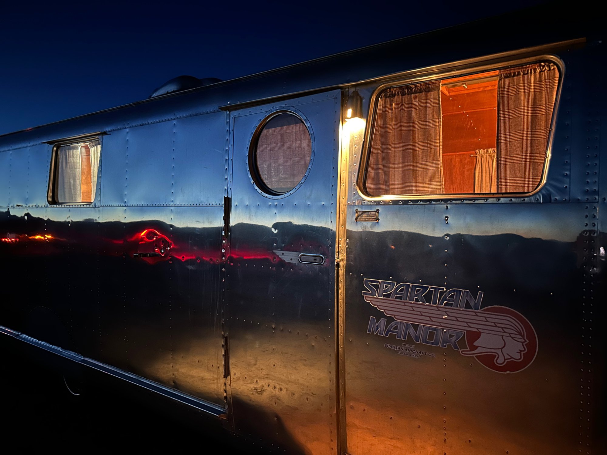 1946 Spartan Manor trailer illuminated at night beside a hidden Vermont pond — the Pondside Spartan farm stay at MacIsaac Highland